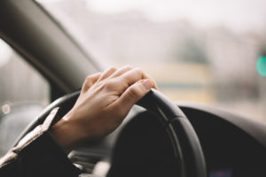 female driver with one hand on steering wheel